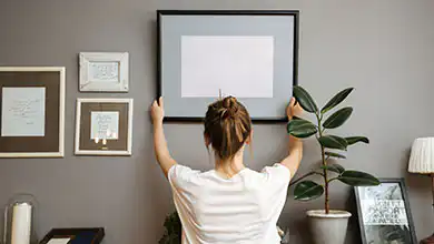 Girl hanging a frame on a gray wall
