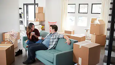 Happy Couple Resting On Sofa Surrounded By Boxes In New Home On